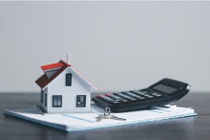 small model of home, calculator and house keys on top of documents